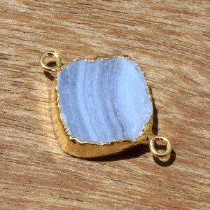 May include: A light blue agate gemstone with gold-toned metal accents. The gemstone is in the shape of a rectangle with rounded edges. The gemstone is set in a gold-toned metal frame. The gemstone is a connector for jewelry making.