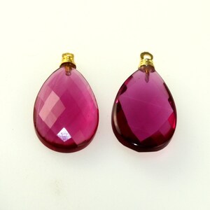 May include: Two faceted, teardrop-shaped pendants. The pendants are a deep magenta color with gold-colored metal caps. The facets create a sparkling effect. These pendants are suitable for jewelry making.
