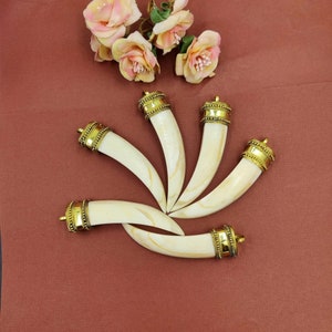 May include: Five white, curved pendants with gold accents. The pendants are arranged in a circle on a brown background.