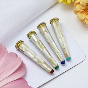 May include: Four decorative smoking pipes. Each pipe has a white mother-of-pearl mosaic design, a gold-coloured metal cap, and a coloured gemstone tip. The gemstones are red, green, blue, and turquoise.