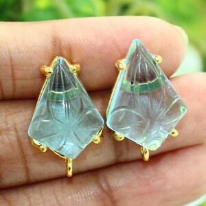May include: A pair of light blue glass earrings with gold accents. The earrings are shaped like a diamond with a carved design.