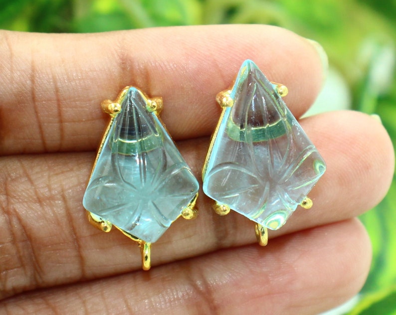 May include: A pair of light blue glass earrings with gold accents. The earrings are shaped like a diamond with a carved design.