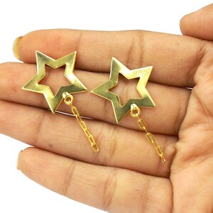 Puede incluir: Un par de pendientes de estrella dorada con una cadena colgante. Los pendientes están hechos de metal y tienen un diseño de estrella hueca.