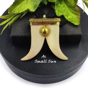 May include: A gold pendant with a sun design and a white bone-like shape. The pendant is on a black surface with the text "A. Small Sun".