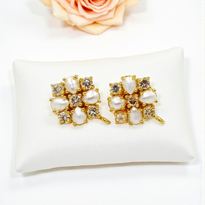 May include: A pair of gold-toned stud earrings. Each earring features a cluster of white, pear-shaped faux pearls and clear, round and square-cut crystals. The earrings are displayed on a white pillow.