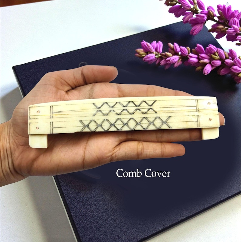 May include: A rectangular comb cover with a cream-colored base and a geometric design in black. The text "Comb Cover" is visible in the image. The comb cover is held in a hand.