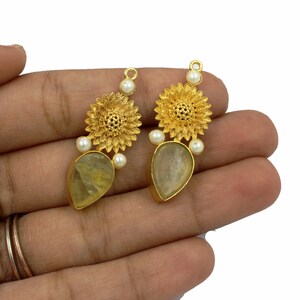 May include: Gold tone earrings with a teardrop shaped clear stone and a floral design with white pearls.
