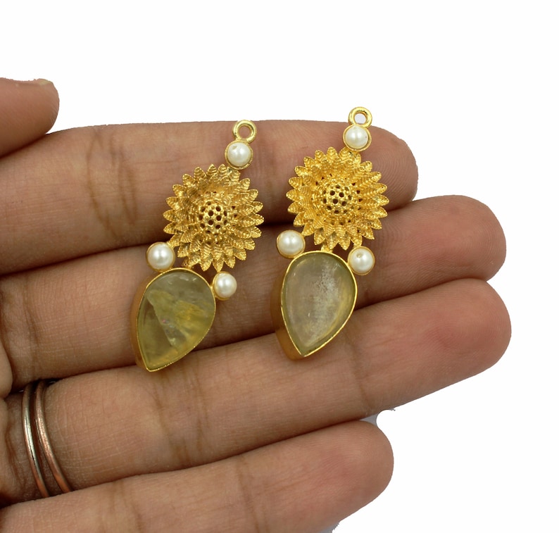 May include: Gold tone earrings with a teardrop shaped clear stone and a floral design with white pearls.