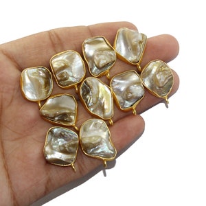 May include: Ten gold-toned metal charms with a pearlescent finish. Each charm has a different shape and features a unique pattern.