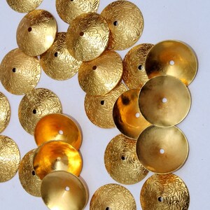 May include: A collection of gold-colored metal embellishments with a decorative floral pattern. The embellishments are round and have a raised center.