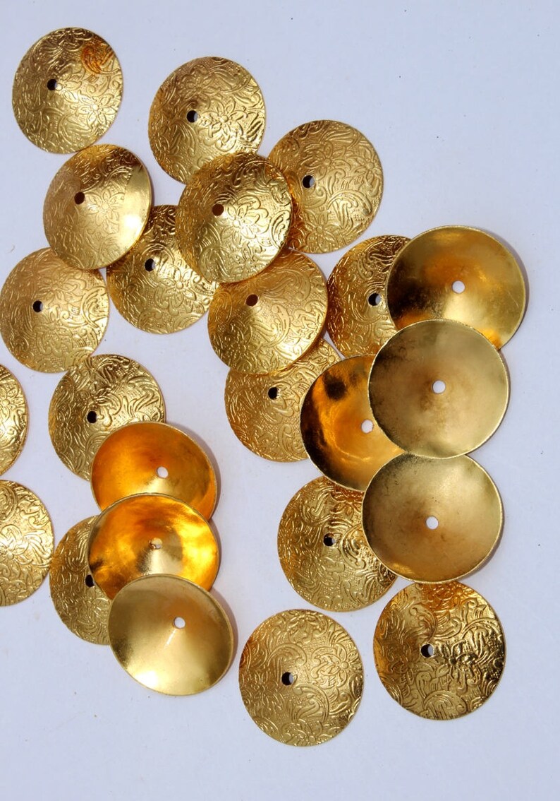 May include: A collection of gold-colored metal embellishments with a decorative floral pattern. The embellishments are round and have a raised center.