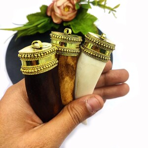 May include: Three pendants made from animal teeth with gold-colored metal caps. The teeth are different colors: dark brown, light brown, and white.