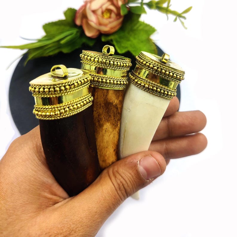 May include: Three pendants made from animal teeth with gold-colored metal caps. The teeth are different colors: dark brown, light brown, and white.