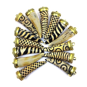 Peut inclure: Un ensemble de 14 pendentifs en corne avec des embouts dorés. Chaque pendentif est sculpté dans l'os et présente un motif géométrique noir et blanc unique.