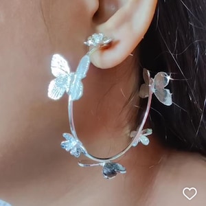 Puede incluir: Pendientes de aro plateados con dise&ntilde;o de mariposa. Los pendientes est&aacute;n hechos de metal y tienen un acabado pulido.