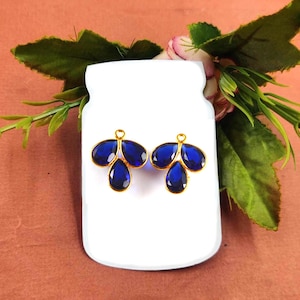 Könnte beinhalten: Ein Paar goldfarbene Ohrring-Verschlüsse mit drei blauen tropfenförmigen Kristallen.