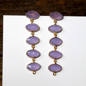 May include: A pair of long, gold dangle earrings with five lavender oval-shaped gemstones on each earring.