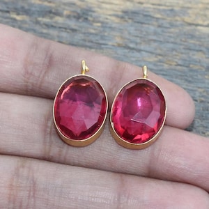 May include: Two oval-shaped pink glass pendants with gold-toned metal settings. The pendants have a faceted design and are perfect for jewelry making.