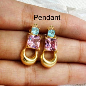 Puede incluir: Dos colgantes de oro con un diseño de piedra preciosa cuadrada azul claro y rosa. El colgante tiene un bucle en la parte superior para sujetarlo a una cadena o pulsera. La palabra "Colgante" está escrita encima de los colgantes.