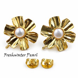 May include: A pair of gold-toned flower-shaped earrings featuring a central white freshwater pearl. Each earring has a textured, petal-like design and a small loop at the bottom. Two matching gold-toned earring backs are included below the earrings.