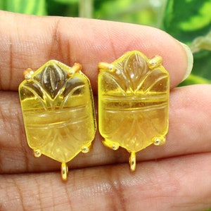 May include: Two yellow glass pendant charms with gold-tone metal accents. The charms are rectangular and feature a carved design.