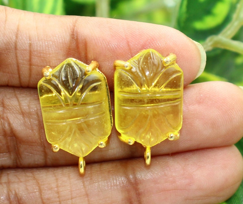 May include: Two yellow glass pendant charms with gold-tone metal accents. The charms are rectangular and feature a carved design.