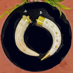 May include: Two white bone pendants with gold accents. The pendants are shaped like a curved tusk with a gold cap on one end and gold dots along the side. The pendants are labeled A and B.