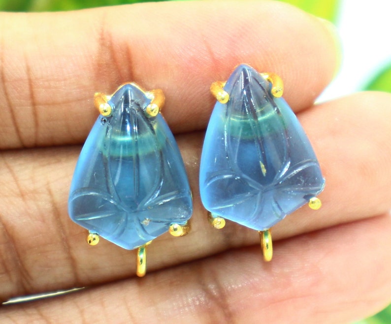 May include: A pair of blue teardrop-shaped earrings with gold accents. The earrings have a carved floral design and are attached to a gold hook.