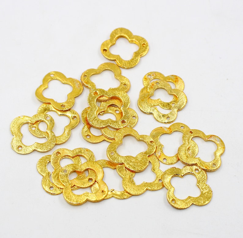 May include: A group of 14 gold-colored metal flower-shaped charms with a textured surface. Each charm has four rounded petals and a hole in the center.