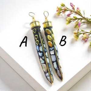 May include: A pair of long, decorative earrings with a black base, gold detailing, and iridescent mosaic inlays. One earring has teardrop-shaped green gems, the other gold leaf-shaped details. The earrings are labelled A and B.
