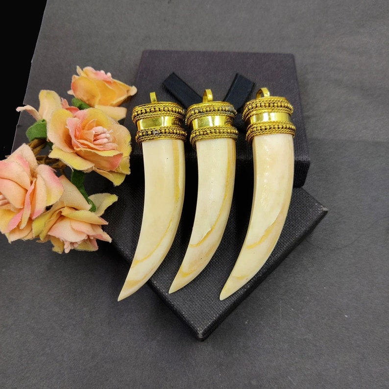 May include: Three gold-trimmed ivory pendants shaped like tusks. The pendants are displayed on a black velvet background.