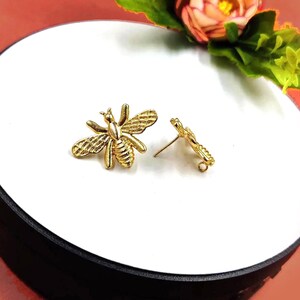 May include: A pair of gold bee stud earrings. The bee is detailed with a textured body and wings.