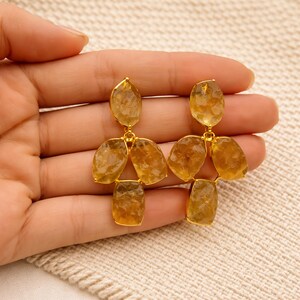 May include: Gold-toned earrings featuring clusters of faceted, amber-colored gemstones. The earrings have a three-dimensional design, with each earring composed of multiple stones connected by delicate gold links. The gemstones have a natural, irregular shape.
