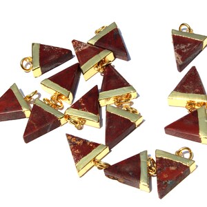 Puede incluir: Una colección de 12 colgantes de forma triangular roja y dorada. Los colgantes están hechos de jaspe rojo con un borde chapado en oro. Cada colgante tiene un anillo de salto dorado para sujetarlo a una cadena o cordón.