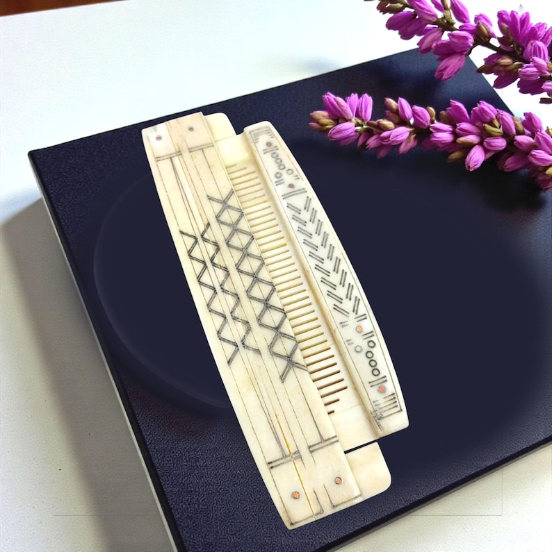 May include: Two antique ivory-colored combs with intricate geometric designs. One comb features a series of intersecting lines, while the other has a pattern of diagonal lines and circles. The combs are displayed on a dark blue surface, with purple flowers in the background.