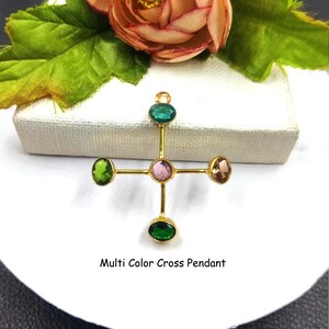 Puede incluir: Un colgante de cruz dorada con cinco piedras preciosas de colores. Las piedras preciosas son verdes, rosas y marrones. El texto "Multi Color Cross Pendant" est&aacute; debajo.