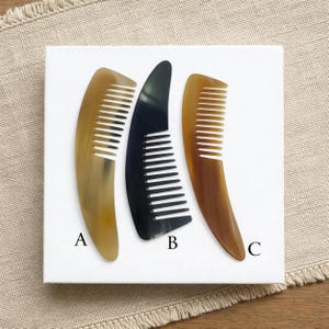 May include: Three horn combs in varying shades of brown and black are displayed on a white surface. The combs are labeled A, B, and C. Comb A is light brown, B is black, and C is dark brown. The combs have fine teeth.