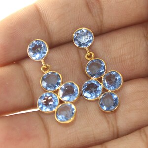 May include: Gold dangle earrings with multiple light blue round gemstones.