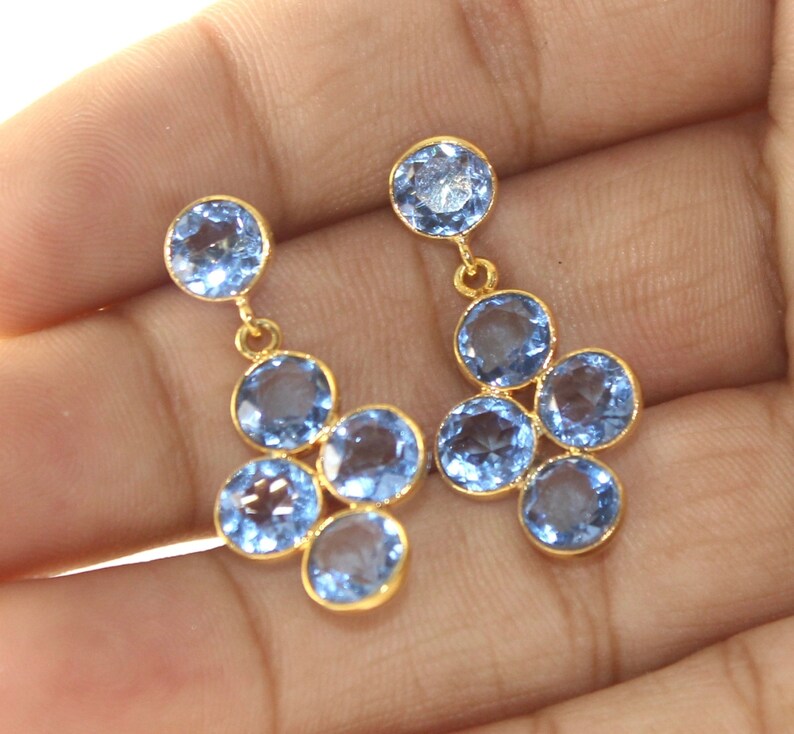 May include: Gold dangle earrings with multiple light blue round gemstones.