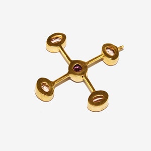 Puede incluir: Colgante dorado con dise&ntilde;o de cruz. Cuenta con cuatro piedras ovaladas de color claro en los extremos y una peque&ntilde;a piedra redonda morada en el centro. El colgante se encuentra sobre un fondo blanco.