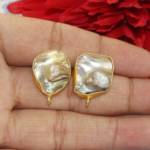 May include: Two gold-toned metal earring findings with a white and brown iridescent shell inlay. The shell has a natural, organic shape.