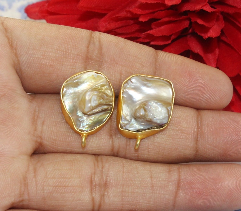 May include: Two gold-toned metal earring findings with a white and brown iridescent shell inlay. The shell has a natural, organic shape.