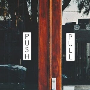 May include: A pair of glass doors with wooden frames. The left door has a sign that says "PUSH" and the right door has a sign that says "PULL".