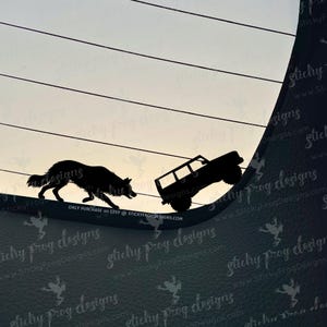 May include: Silhouette decal featuring a black dog and a 4x4 vehicle climbing a hill. The background shows a gradient sky. Text at the bottom reads "ONLY PURCHASE on ETSY @ STICKYFROGDESIGNS.COM".