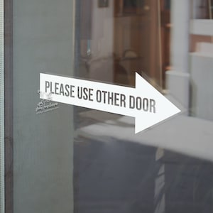 May include: White arrow sign on a glass door that reads "PLEASE USE OTHER DOOR".