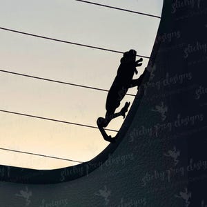 May include: A black silhouette of a frog climbing a curved surface, possibly a car window or a similar structure. The background shows a gradient of colors, transitioning from a light sky to a darker shade. The text "sticky frog designs" is visible.
