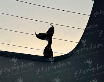 May include: A black whale tail silhouette against a light background with horizontal lines. The tail is curved and detailed, suggesting a marine theme. The image has a minimalist design, suitable for decals or stickers.