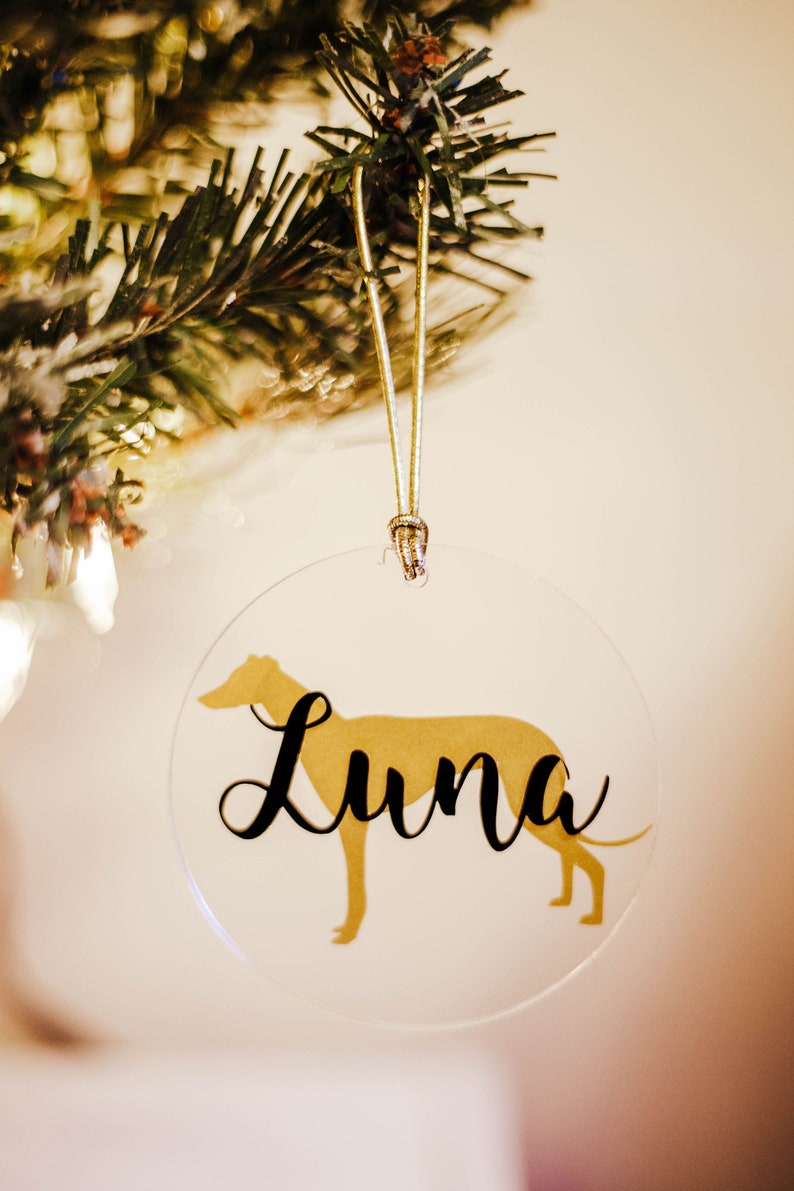 May include: A clear round Christmas ornament with a gold silhouette of a dog and the name "Luna" written in black cursive.