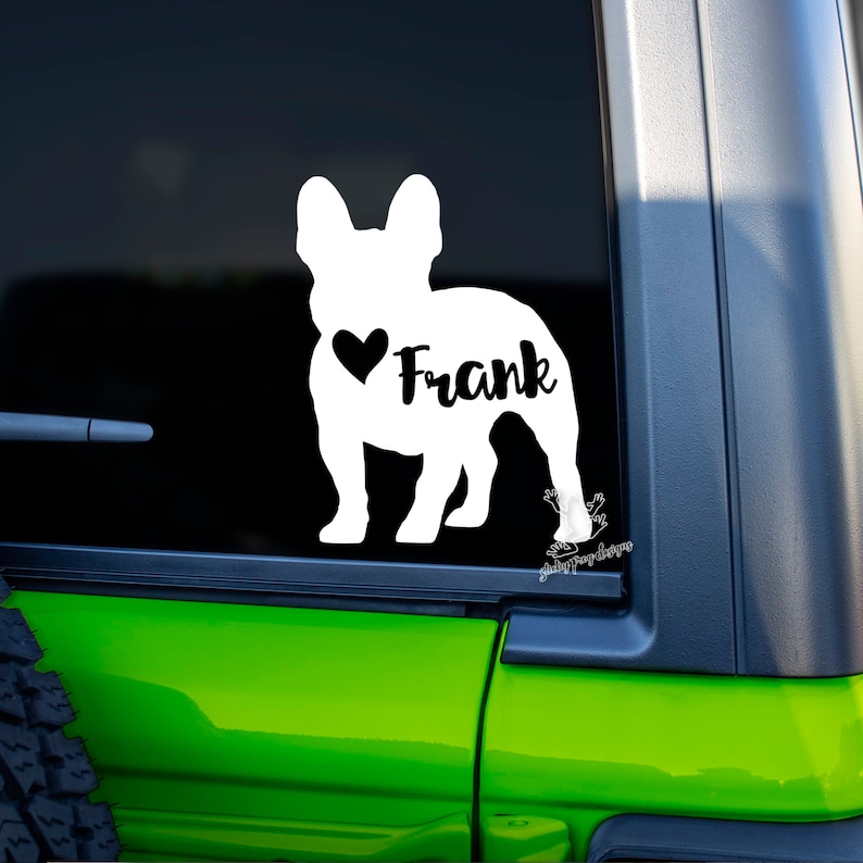 Puede incluir: Calcoman&iacute;a de vinilo blanco con la silueta de un Bulldog Franc&eacute;s con un coraz&oacute;n y el nombre "Frank" en la ventana de un coche verde.