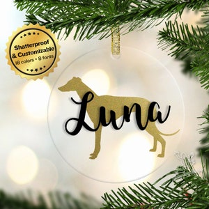May include: A clear glass Christmas ornament with a gold glitter Greyhound silhouette and the name "Luna" in black script.